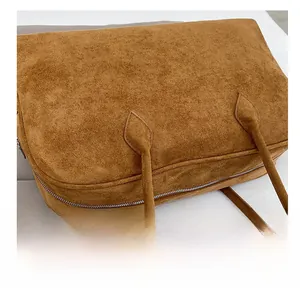Detailed close-up of tight stitching and silver zipper on a brown suede tote bag
