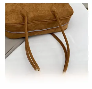 Close-up of the dual shoulder straps and metal zipper on a brown suede Boston bag