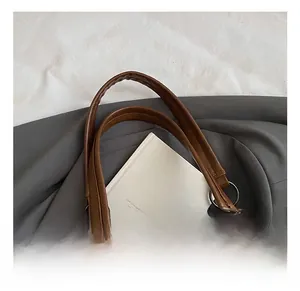 Detail of a brown PU tote bag showing silver metal ring buckles and striped bag charm
