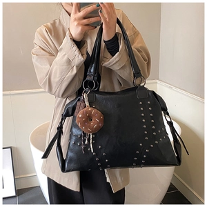 Detail of black faux leather tote bag featuring silver studs and a donut charm