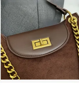 Detail der braunen Wildledertasche mit goldenem Drehverschluss und Metallkette