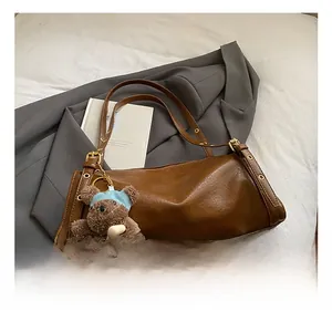 Detail of brown PU leather tote bag with pleated texture and plush bear pendant accessory