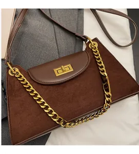 Detail einer braunen Wildleder-Umhängetasche mit Goldkette und quadratischem Drehverschluss