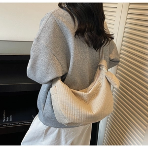 Detail of beige pleated crescent bag texture and zipper closure shown on a model
