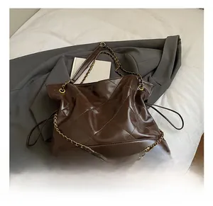 Detail of coffee brown quilted tote bag with gold chain strap on a white surface