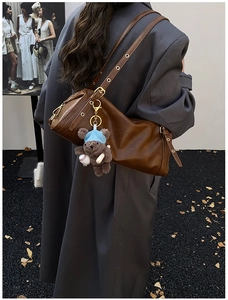 Detail of vintage brown leather tote bag with cute bear charm worn on shoulder over a grey blazer