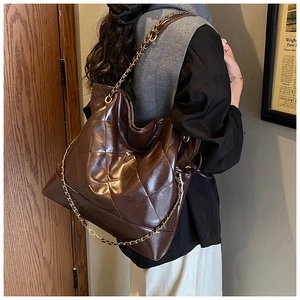 Close-up of brown quilted tote bag with gold chain strap on model's shoulder