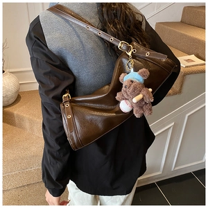 Detail of dark brown retro leather shoulder bag featuring a cute plush bear pendant