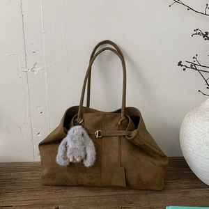 Minimalist large brown suede tote bag with plush rabbit charm on a wooden table