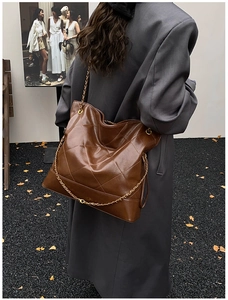 Detail of a large brown quilted tote bag with chain strap on a model wearing a grey coat
