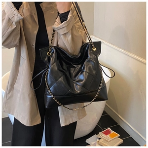 Classic black quilted tote bag with metal chain strap shown on a model in a cozy setting