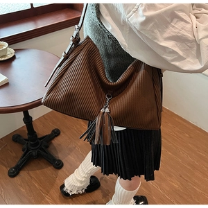 Close-up of brown pleated hobo bag with fringe pendant and adjustable strap on a model