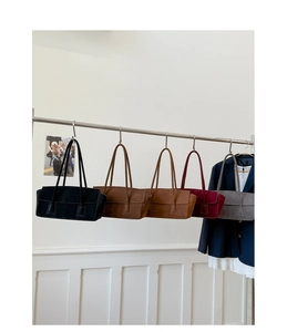 Detail showing five colors of minimalist suede shoulder bags on a metal display rack
