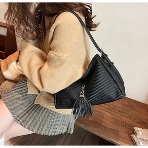 Detail of black pleated shoulder bag with long strap and matching tassel charm