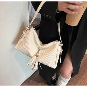 Detail of a pleated cream tote bag with leather tassel on a model in a black blazer