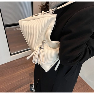 Detail der cremefarbenen Cord-Schultertasche mit Faltenstruktur und Quastenanhänger