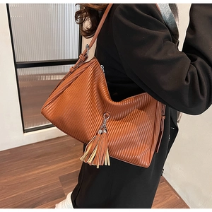 Detail view of a brown pleated tote bag with tassels worn over a black winter coat