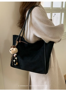Close-up of black suede tote bag with a cute plush puppy pendant and minimalist straps