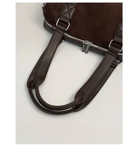 Detail of suede and leather stitching with metal hardware on dark brown tote bag