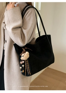 Detail view of a black suede tote bag with a cute teddy bear charm on a beige coat