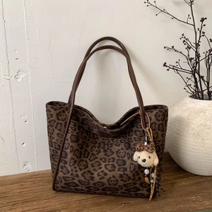 Detailed view of leopard print tote bag with plush puppy pendant on wooden surface