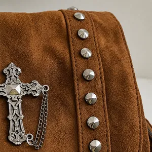 Detail of brown suede bag featuring silver metal rivets and a gothic cross pendant charm