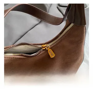 Detailed macro view of the golden metal zipper with logo on a brown suede dumpling bag