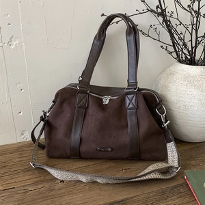 Large dark brown suede tote bag with geometric strap on a minimalist wooden table
