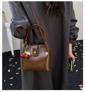 Macro view of a dark brown vintage bucket bag with a cherry pendant and gold clasp