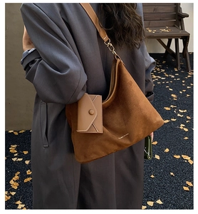 Detail of a brown suede crossbody bag with matching envelope mini pouch and golden hardware