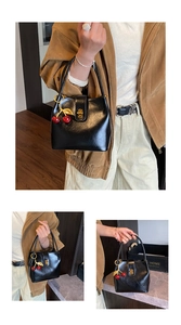 Detail of black leather handbag featuring red cherry charm and gold twist lock