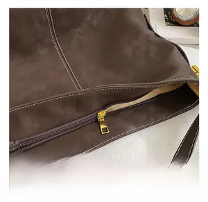 Makro-Detail der dunkelbraunen Wildleder-Beuteltasche mit Kontrastnaht und Goldreißverschluss