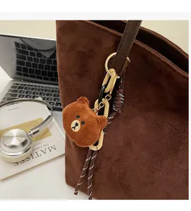 Nahaufnahme von braunem Plüschbär-Anhänger mit Acrylketten an Wildledertasche