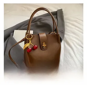 Close-up of brown vintage bucket bag featuring a gold buckle and cherry charm detail
