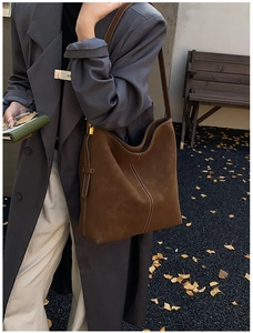 Detail of dark brown suede shoulder bag with contrast stitching and metal buckle side strap