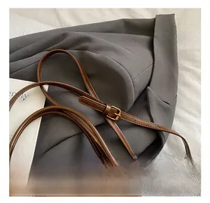 Detail view of the adjustable leather shoulder strap with gold buckle on a brown bucket bag