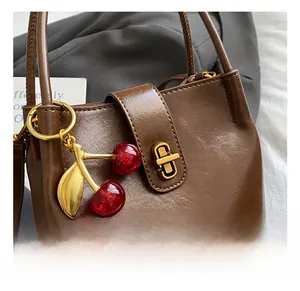 Detail of dark brown leather bucket bag with gold hardware and cherry charm pendant