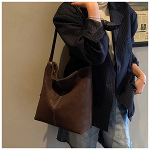 Detail of dark brown matte leather tote bag with white contrast stitching on model