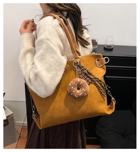 Detail view of large mustard suede tote bag with decorative plush charms on shoulder