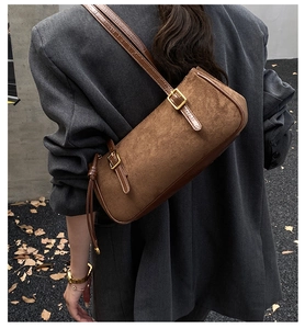 Close-up detail of stylish brown suede shoulder cylinder bag with chic leather strap design.