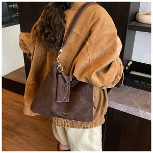 Detail of a dark brown suede tote bag featuring gold lettering and a matching mini pouch