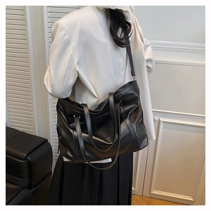 Large black soft leather tote bag worn as a shoulder bag on model in minimalist room