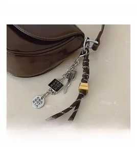 Détail d'un sac en cuir marron foncé avec breloques métalliques et cordon tressé