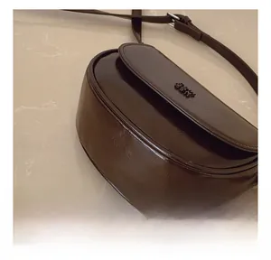 Détail du sac selle marron foncé avec texture plissée brillante et coutures de précision