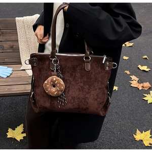 Detail of dark brown suede tote bag with leather handles and donut plush charm