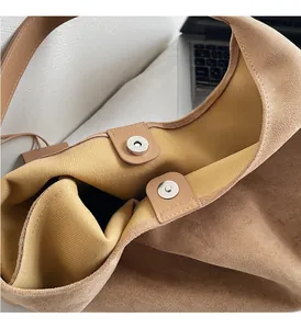 Detail of silver magnetic snaps on a brown suede shoulder bag with striped lining