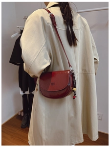 Détail du sac besace bordeaux en cuir poli avec pompon tressé et bandoulière fine