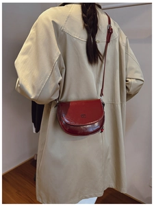 Détail du sac selle bordeaux brillant avec logo embossé sur un trench-coat beige