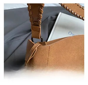 Close-up of brown suede shoulder bag with woven strap and dark metal ring detail