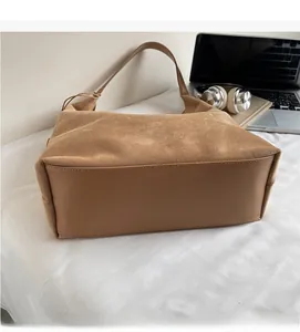 Close-up of brown suede and leather hobo bag with office laptop and headphones